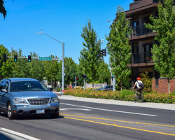 A car travels away from a stoplight as a bicyclist rides on the sidewalk.