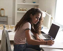 a young girl uses a laptop to study at her desk in bedroom