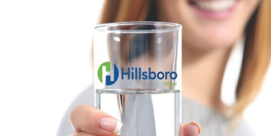 A woman holds a water glass with the Hillsboro Water Department logo