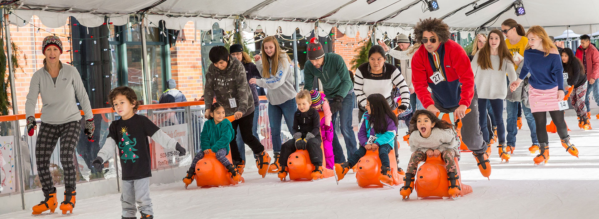 A group of skaters enjoying the ice at Winter Village. Many are pushing young children on bobby ice skating aids.