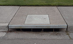 A curb inlet storm drain is a small opening near the edge of the sidewalk and street