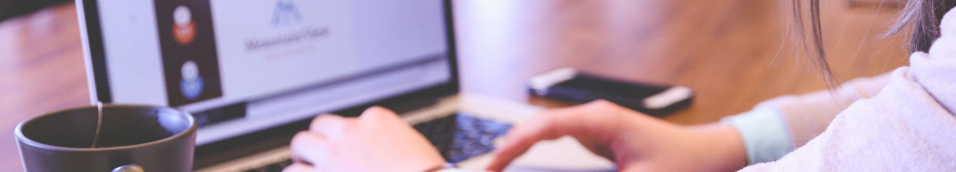 A person works on a laptop with a cup of tea