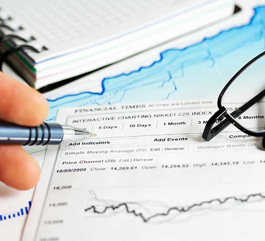 A person looks at a financial chart with a pen, notebook, and glasses nearby