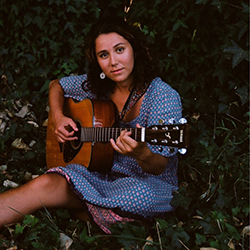 Olivia Klugman plays her acoustic guitar in the woods