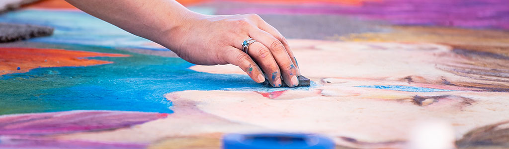 A work of chalk art in progress with the artist's hand visible