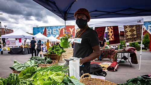 A man sells vegetables at a booth in the Come Thru Market