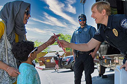 Police officer handing popsicle to mother and child.