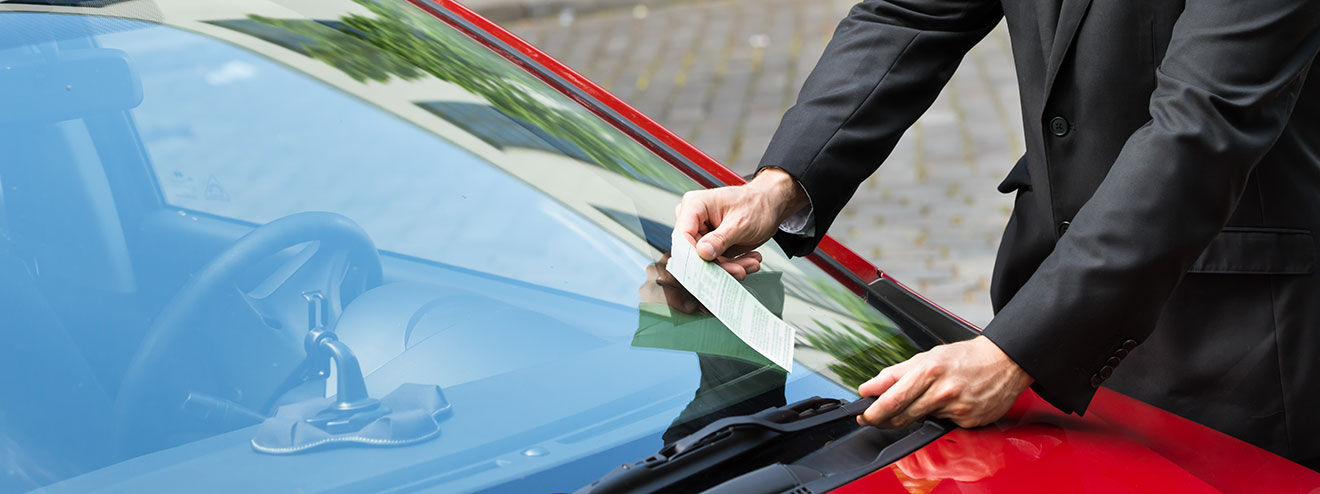 A person collects a parking ticket from their car's windshield