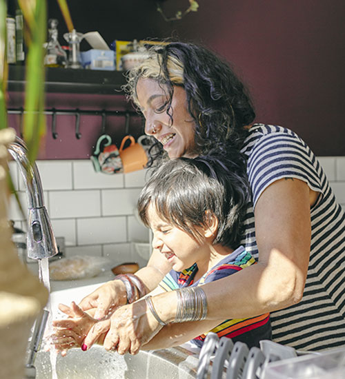 A mother helps her son wash his hands in the kitchen