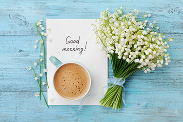 Cup of coffee on a piece of paper that says "Good morning!" next to a bouquet of flowers.