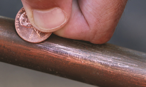 A copper pipe will shine copper when scratched with a coin