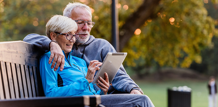 Older couple sitting outside on bench looking at a tablet