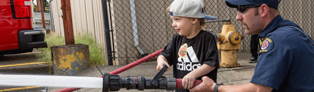 Firefighter guiding child to hold fire hose