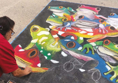 Artists working on a chalk art piece of frogs