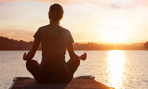 A person meditates near a lake at sunset