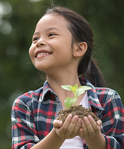 A young girl smiles while holding a seedling