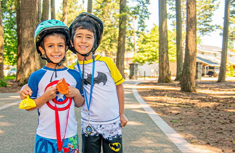 two boys surrounded by trees on a sunny day, wearing superhero t-shirts and helmets, smiling