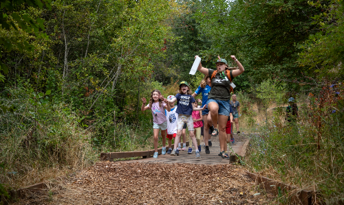 Camp leader and group of kids having fun on nature trail