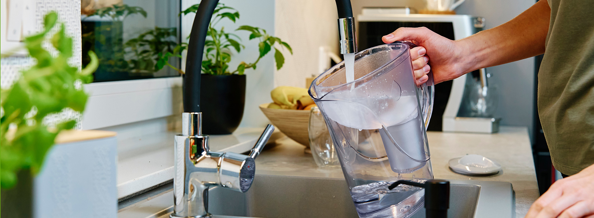 A person fills a pitcher of drinking water at their kitchen sink